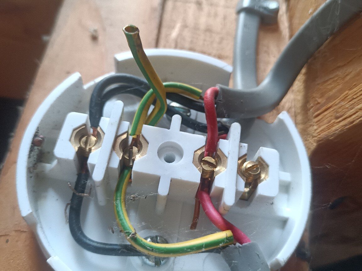 Open junction box showing a disconnected green-and-yellow circuit protective conductor and older socket-circuit wiring