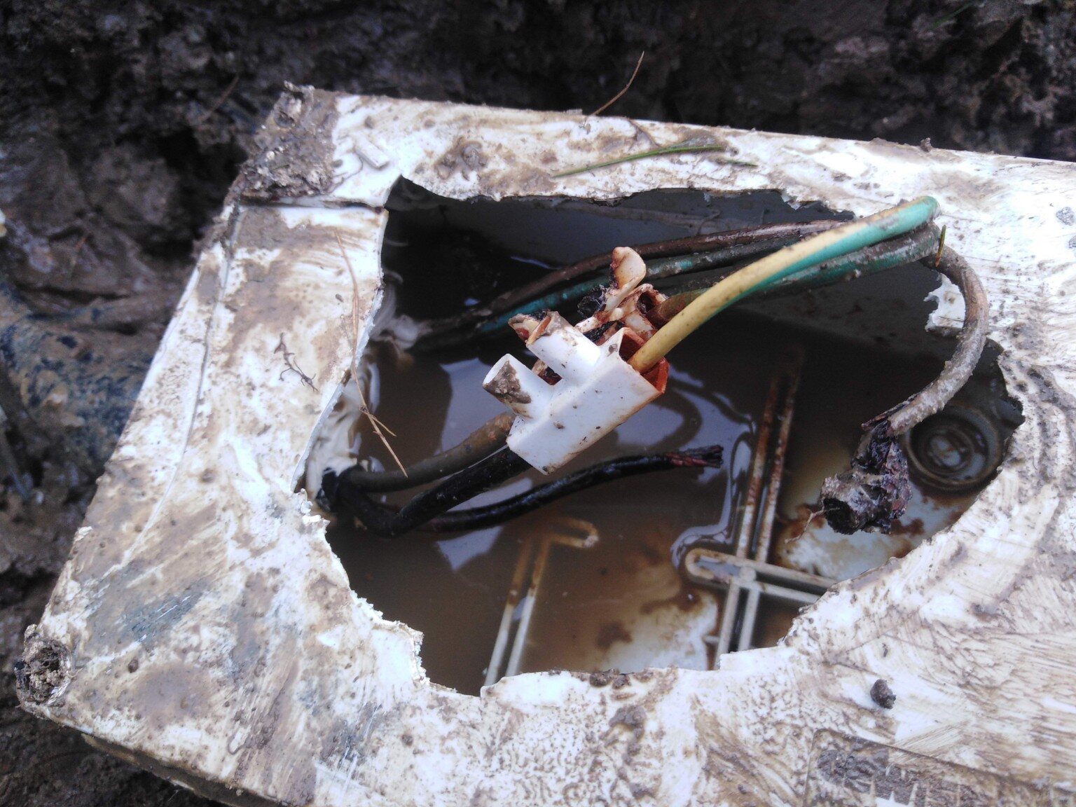 Water inside a buried junction box with a visibly burnt electrical terminal and damaged conductor