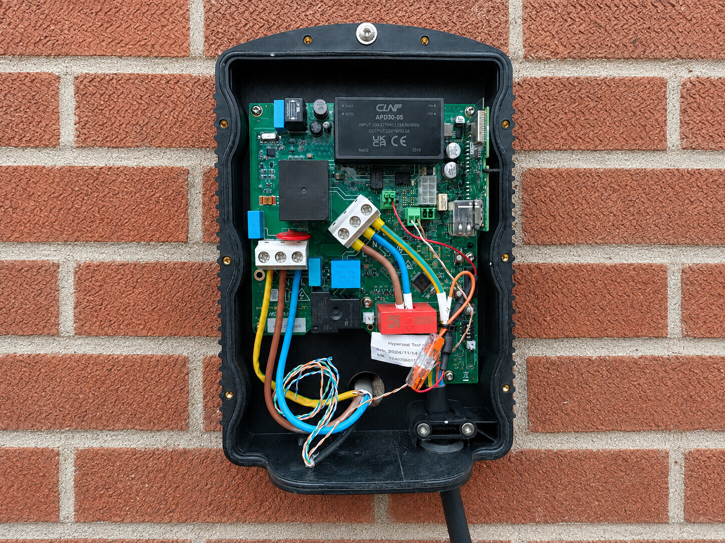 Open EV charge point showing the internal circuit board, wiring, terminals and supply cable during electrical inspection