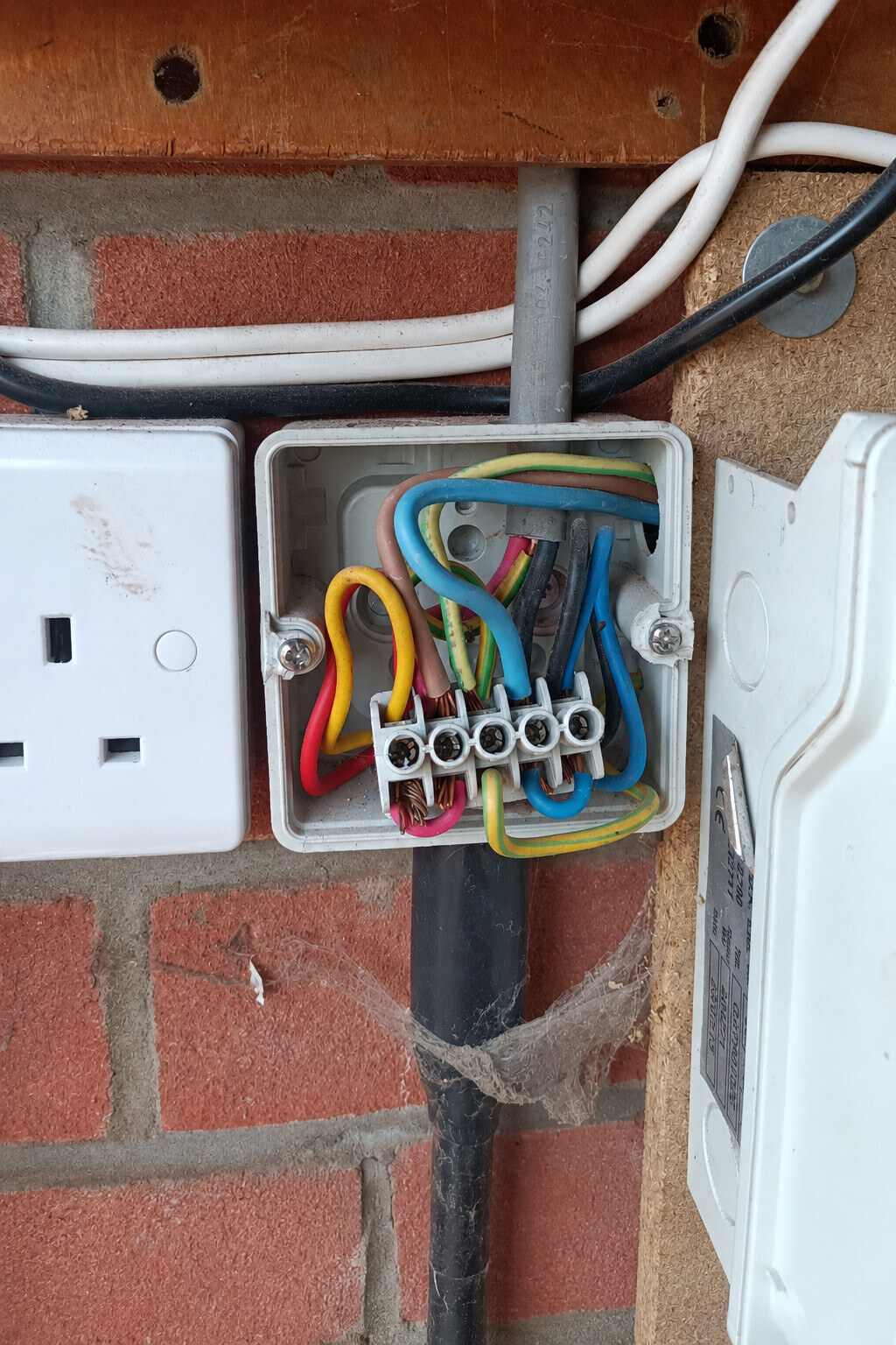 Open junction box showing accessible conductors, a terminal strip and an armoured cable before EICR remedial work